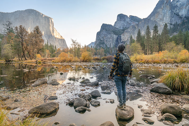 Young man contemplating Yosemite valley from the river, reflections on water surface