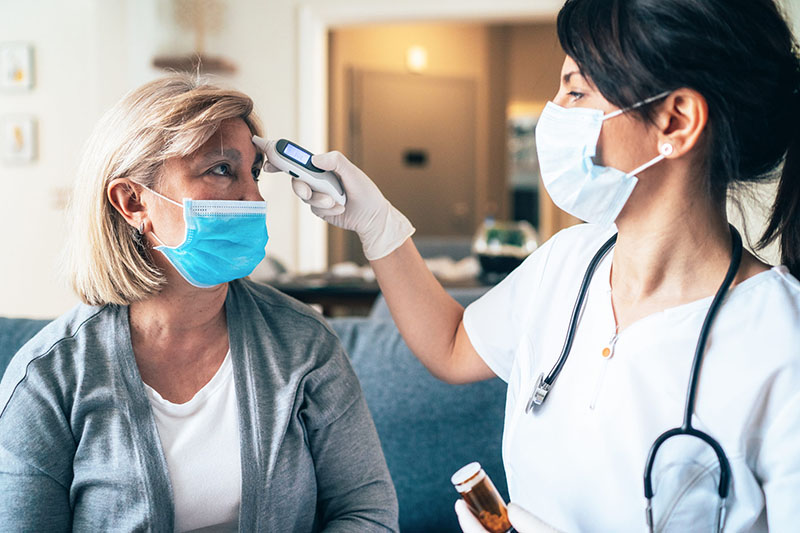 A nurse takes a woman's temperature while both wear face masks